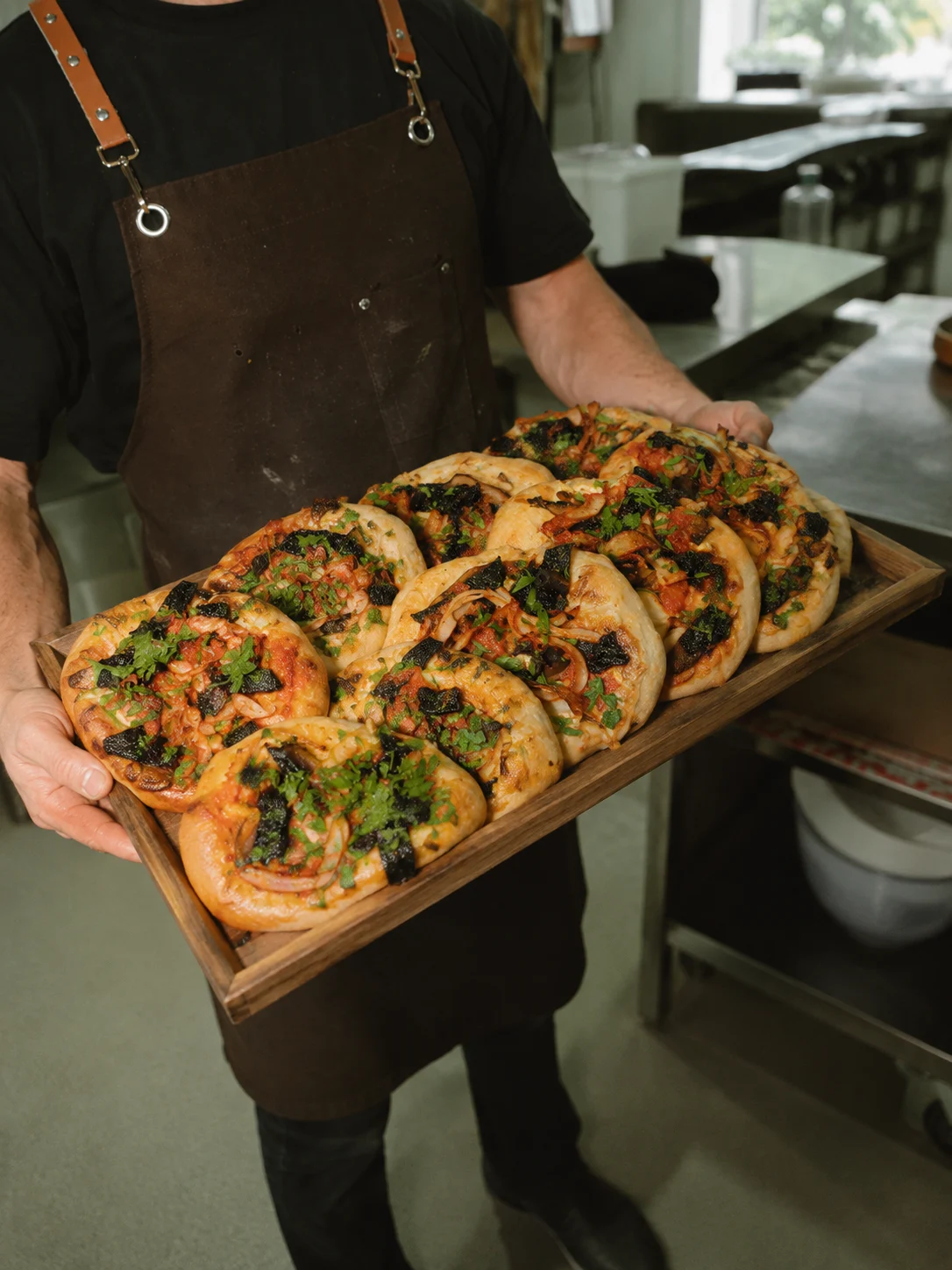 A tray of freshly baked pizzas held by an Eddie's team member